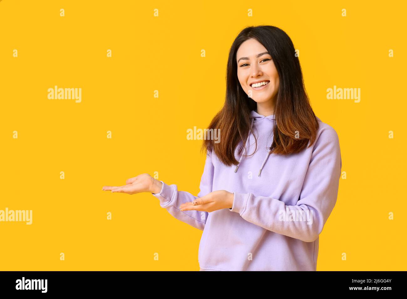 Inviting young Asian woman showing something on yellow background Stock ...