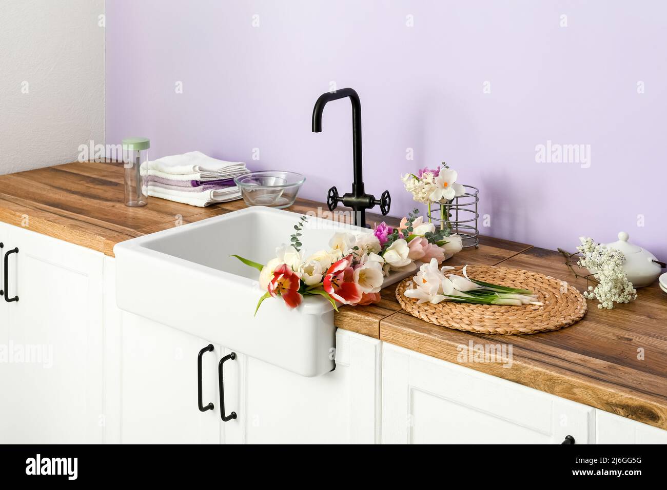 Sink with beautiful flowers and kitchen utensils on counters near lilac