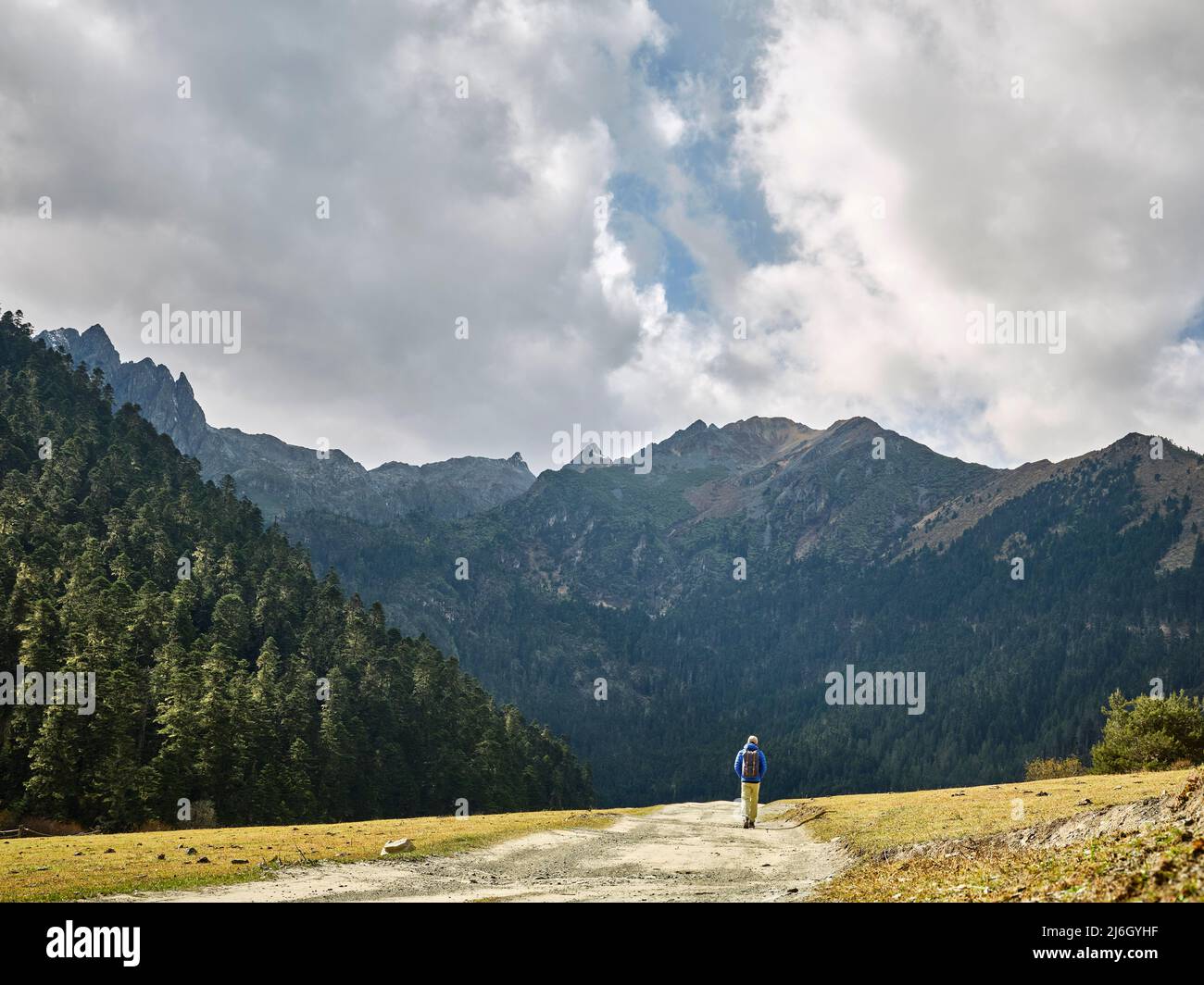 rear view of asian hiker traveler backpacker walking on dirt road towards mountain and forest Stock Photo