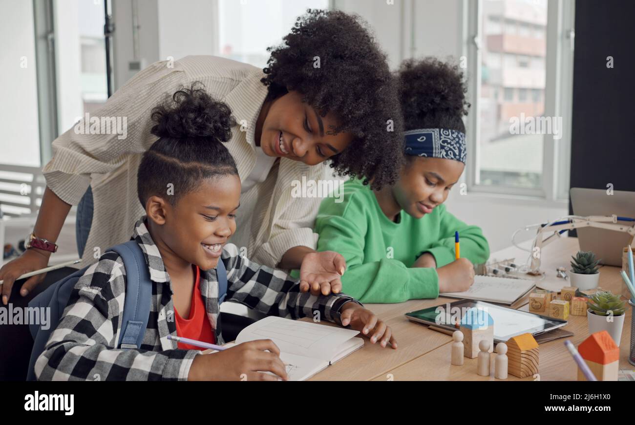 African American female teacher standing with pupils teaching writing lesson in modern classroom. Stock Photo