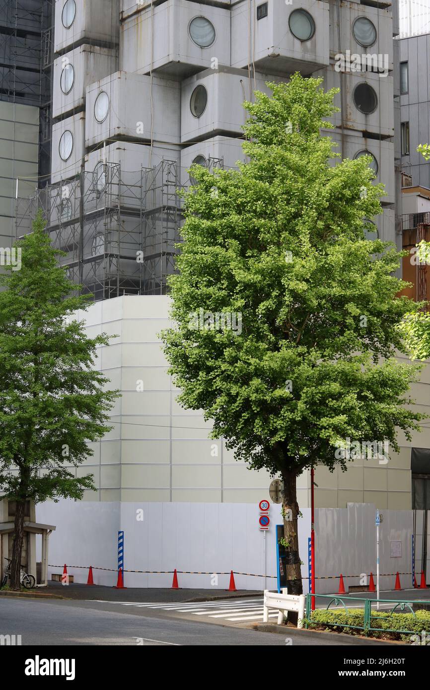 TOKYO, JAPAN - April 28, 2022: View of under-demolition Nakagin Capsule Tower with a fence surrounding the lower section and partitialy covered in sca Stock Photo