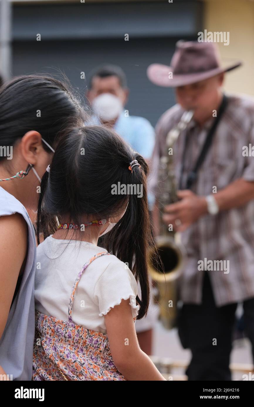 Phuket, Thailand - November 21 2021: Mom and young daughter are enjoying a performance of a street saxophonist Stock Photo