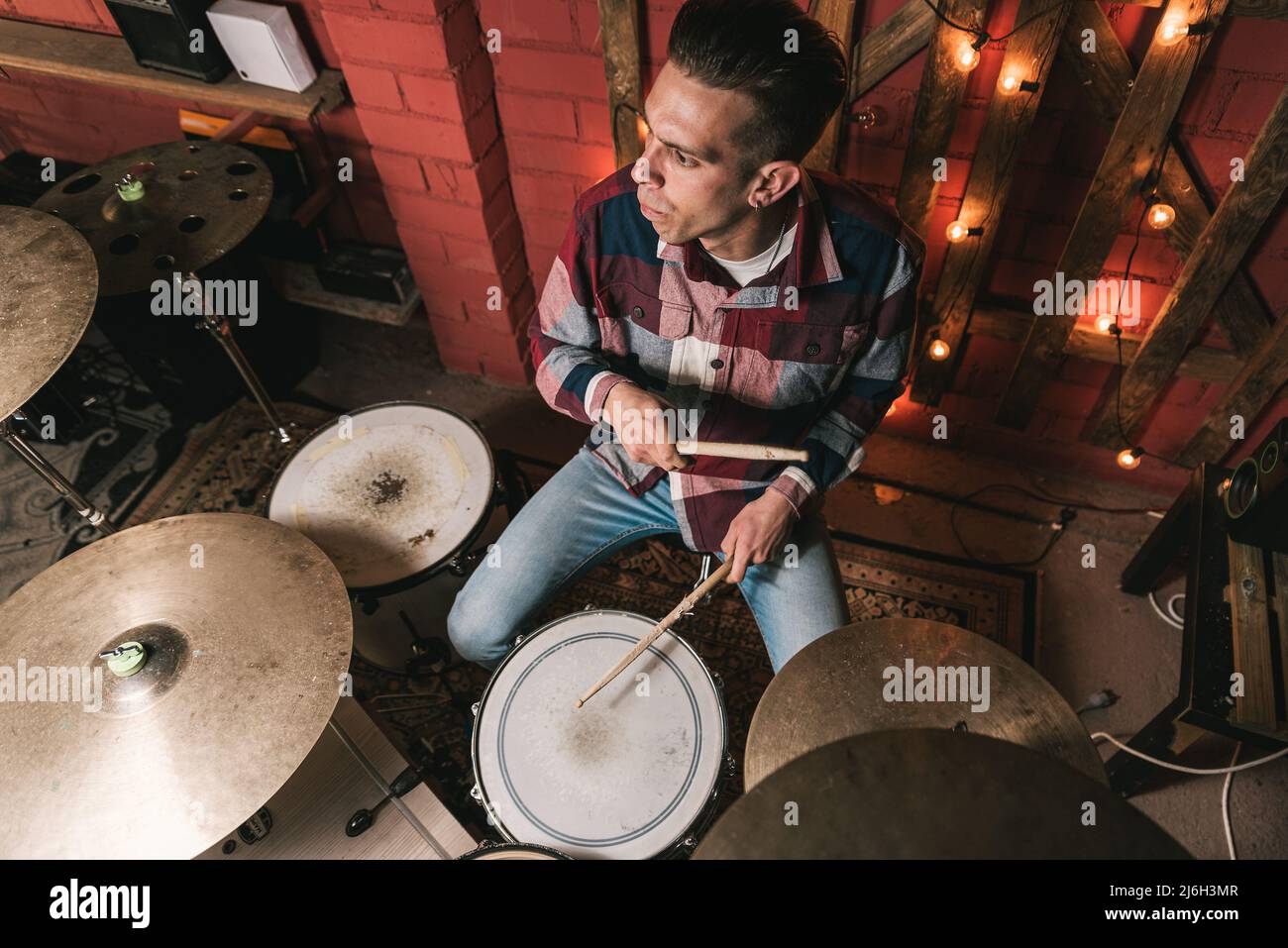 High angle of attentive male drum player performing song on stage during acoustic concert in club Stock Photo