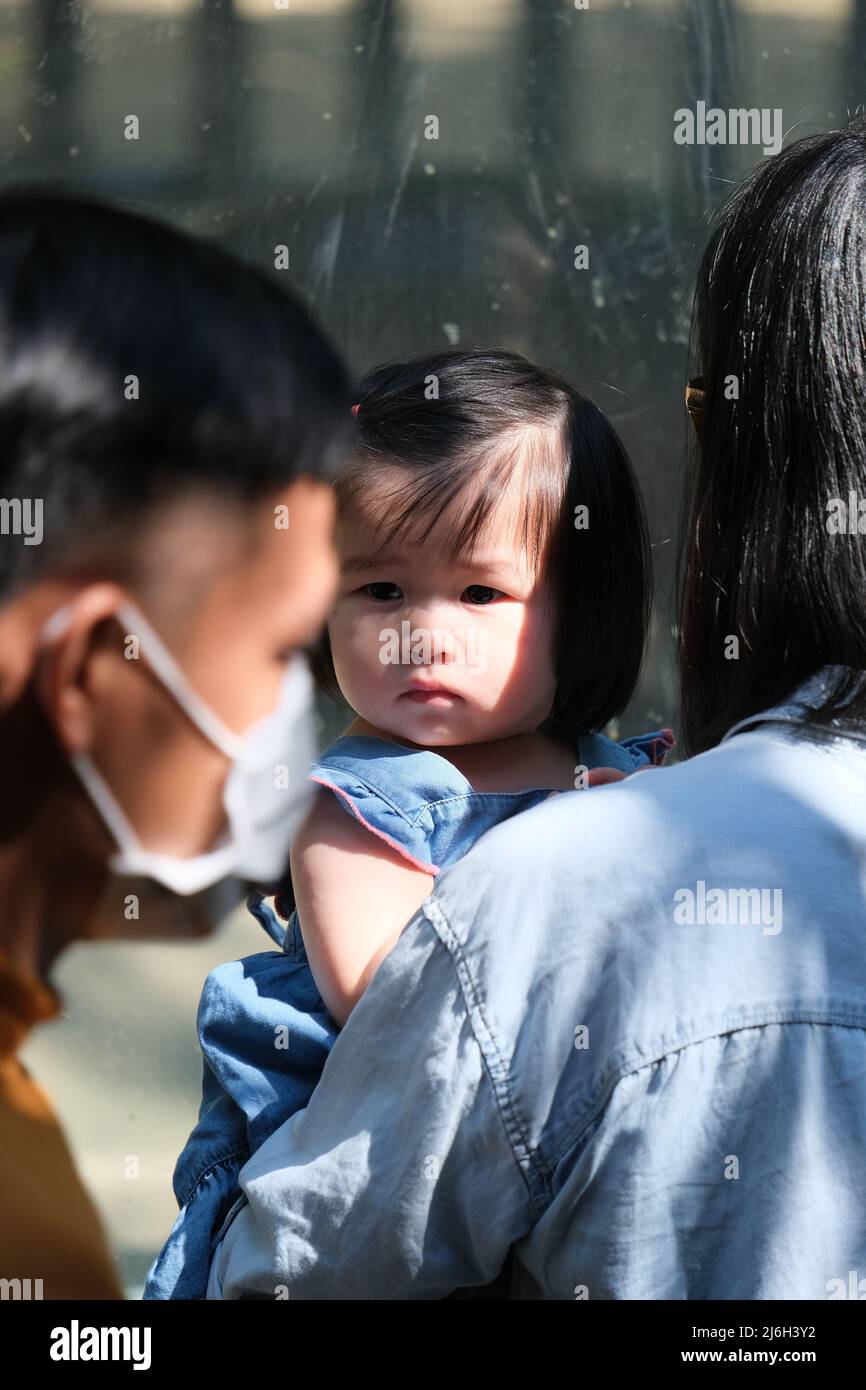 Pattaya, Chonburi / Thailand - December 12 2021: Young Thai girl with a trendy haircut, held by her mom, is looking around while visiting a zoo Stock Photo