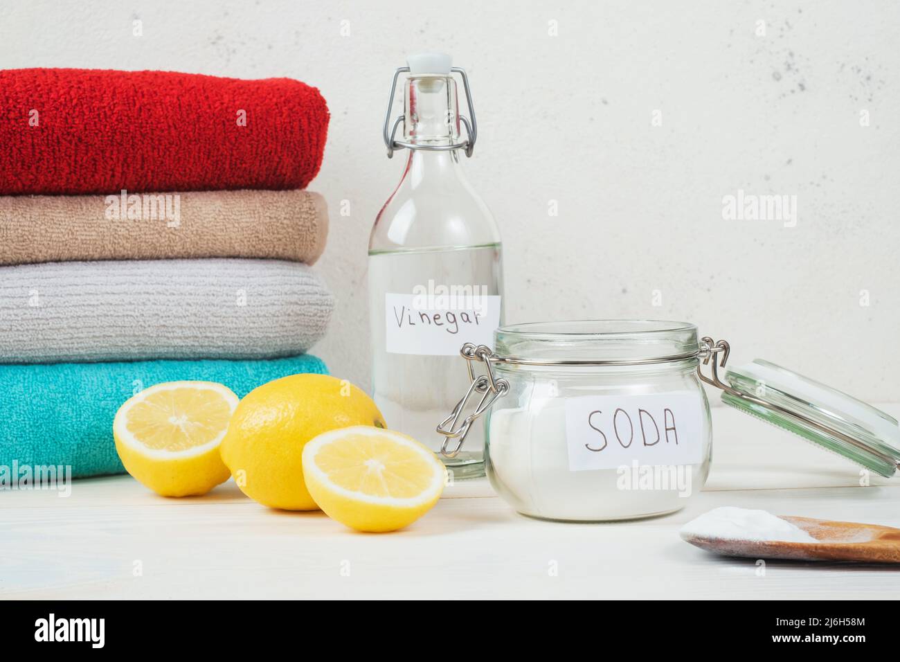 Baking soda in jar, vinegar, cut lemon, folded towel on a white