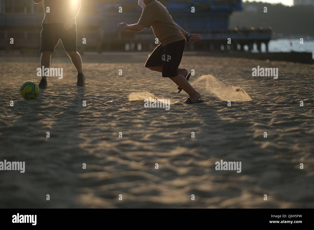 Playing football on the beach, with sand illuminated by sun Stock Photo