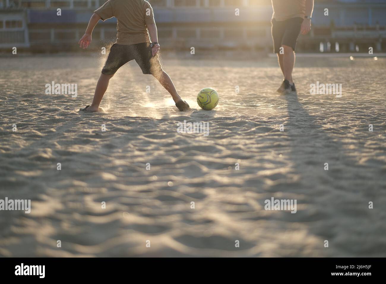 Playing football on the beach, with sand illuminated by sun Stock Photo