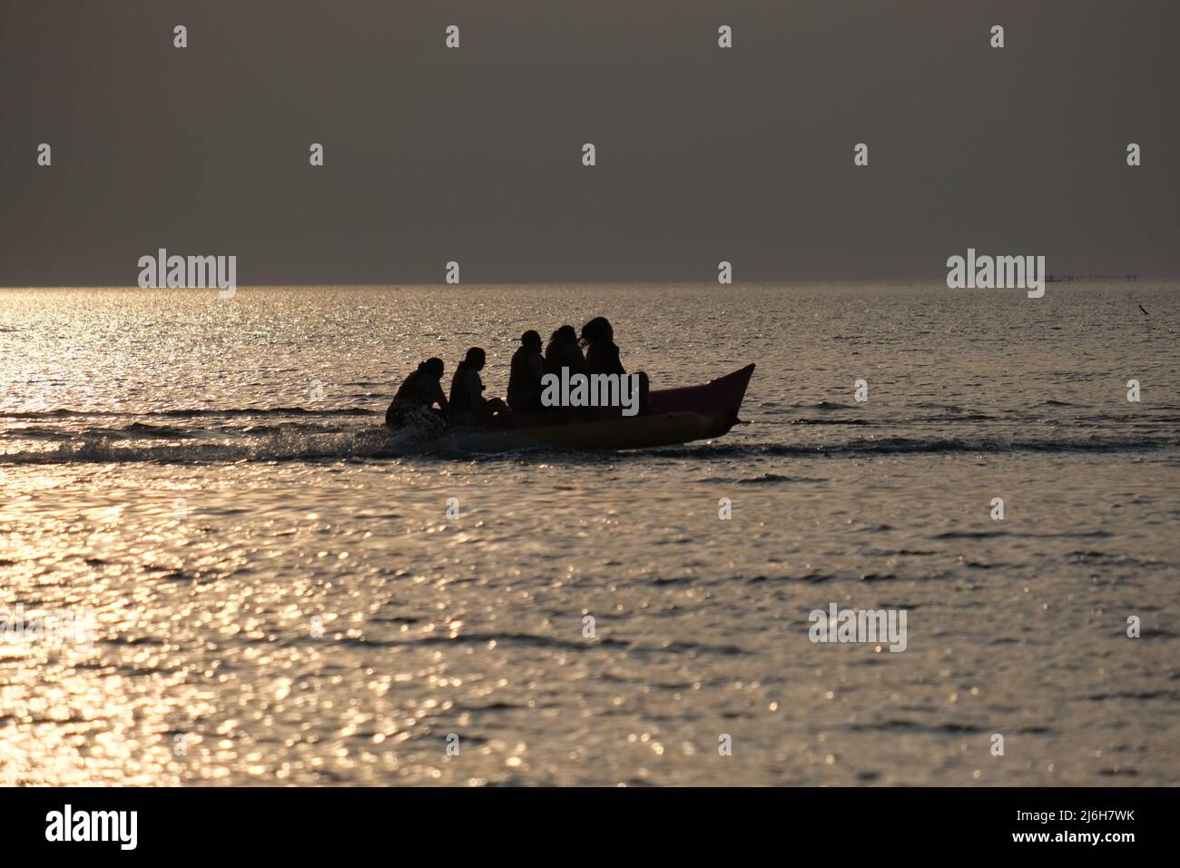 A group of excited tourist is riding a banana boat over brightly lit sea Stock Photo