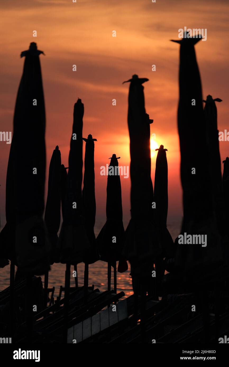 The sun is setting to the sea behind a numerous beach umbrellas folded Stock Photo