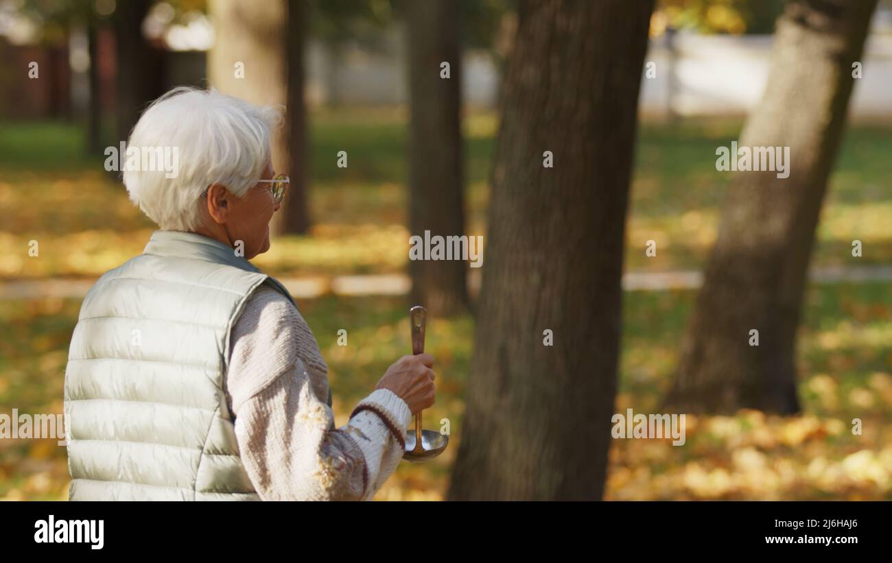 Pensioner caucasian senior charity volunteer lady helping out outdoors in a park by giving soup away to homeless people. High quality photo Stock Photo