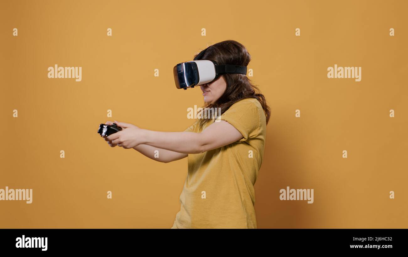 Woman winning difficult level playing game using vr goggles and console controller in studio. Gamer girl having intense experience with virtual reality looking at 3D surrounding enviroment. Stock Photo