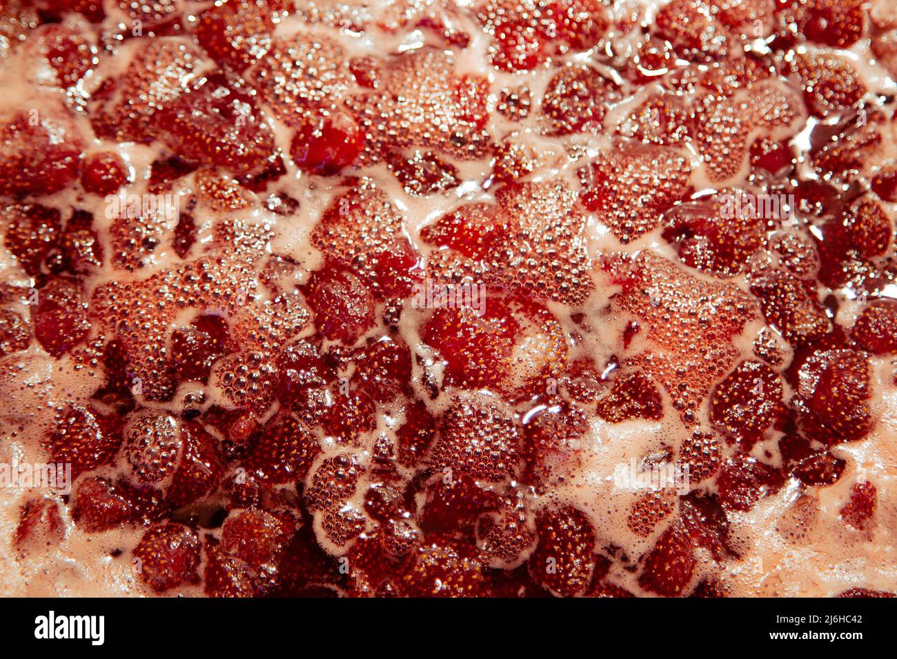 Strawberry jam is boiling, detailed shooting. Close-up of strawberry jelly boiling in a saucepan. Preparation of strawberry jelly, marmalade or strawberry sauce. Stock Photo