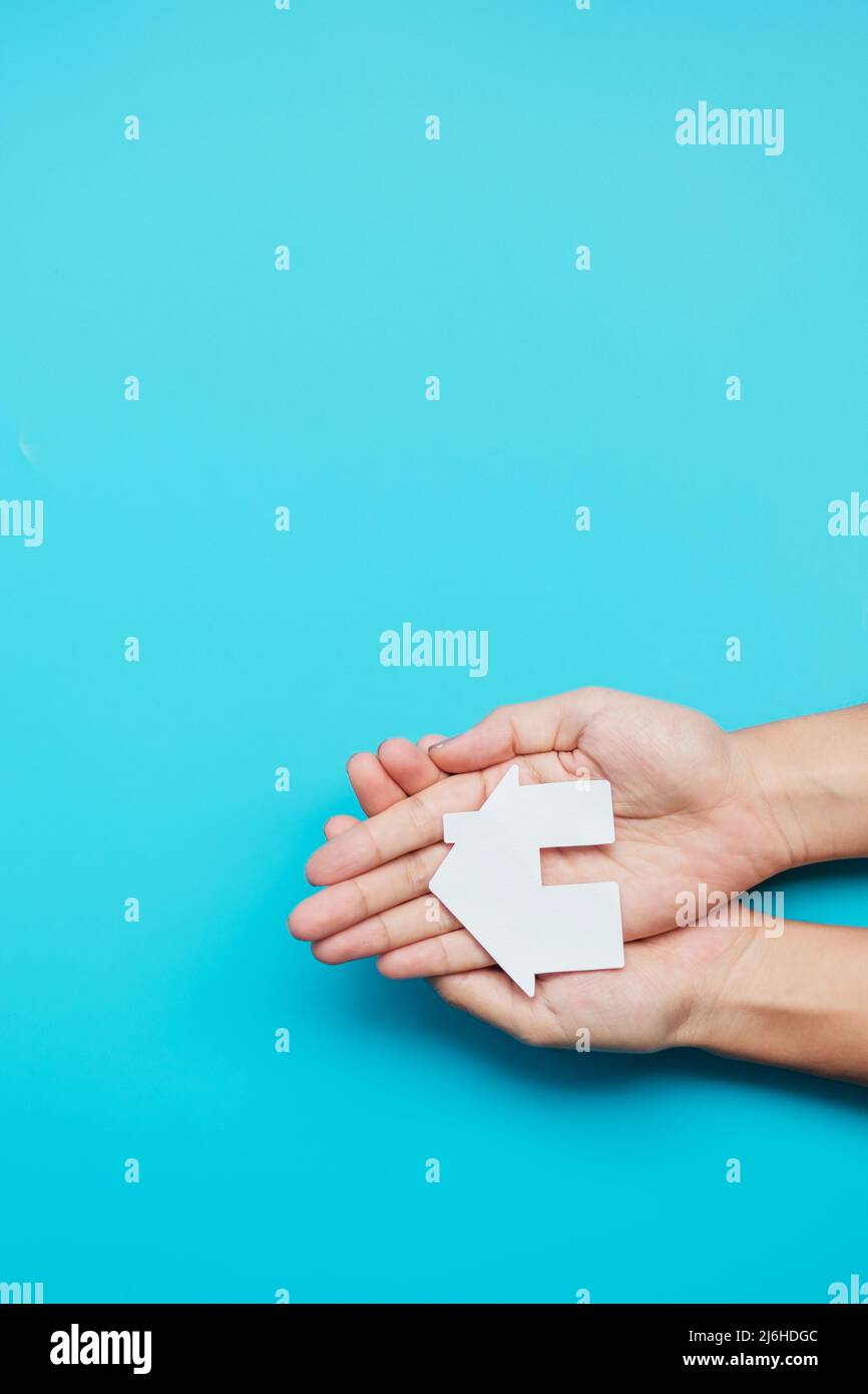hand holding paper Home cutout on blue background. Real estate, Mortgage, Insurance, Rental, Happy Families, Homeless, Foster and Family day concept. Stock Photo