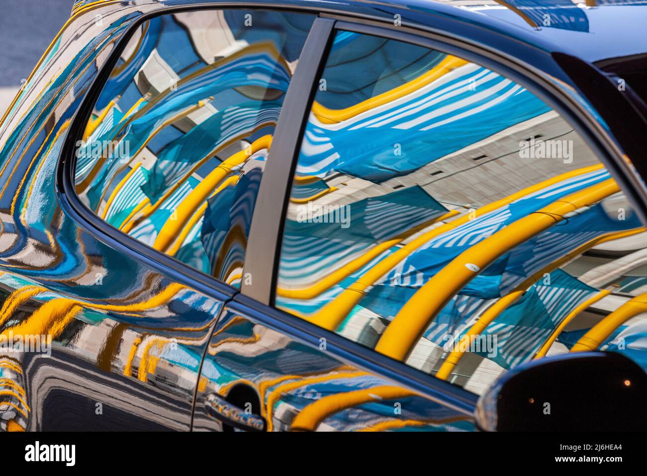 Reflections of yellow pylons and blue flags on a parked car. Brussels