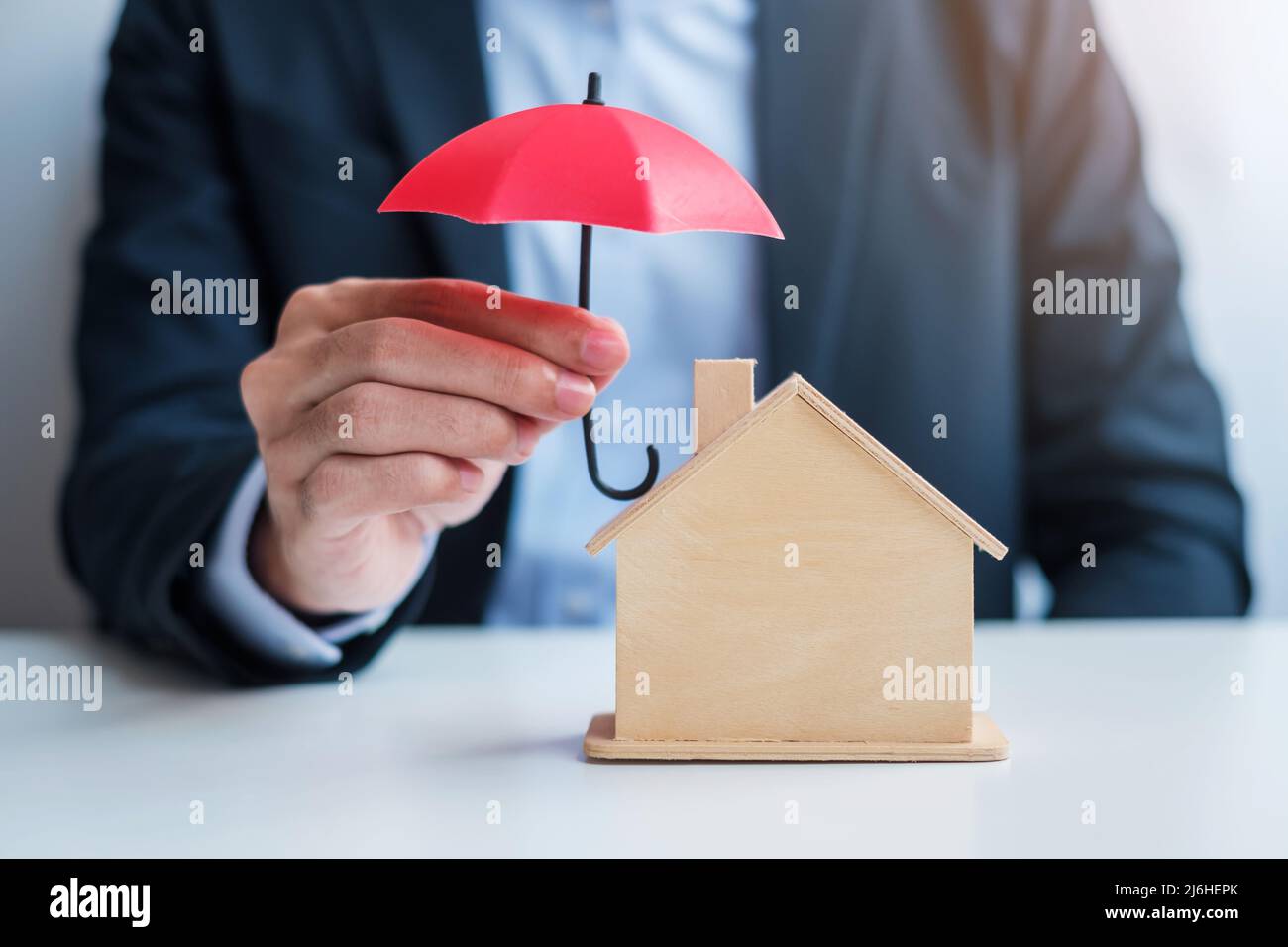 Businessman hand holding red Umbrella cover wooden Home model. real estate, insurance and property concepts Stock Photo