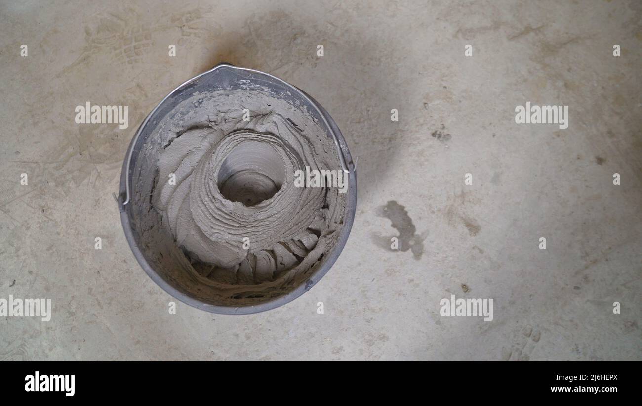 A worker fills a bucket with mortar. Worker mixes the mortar. Worker's