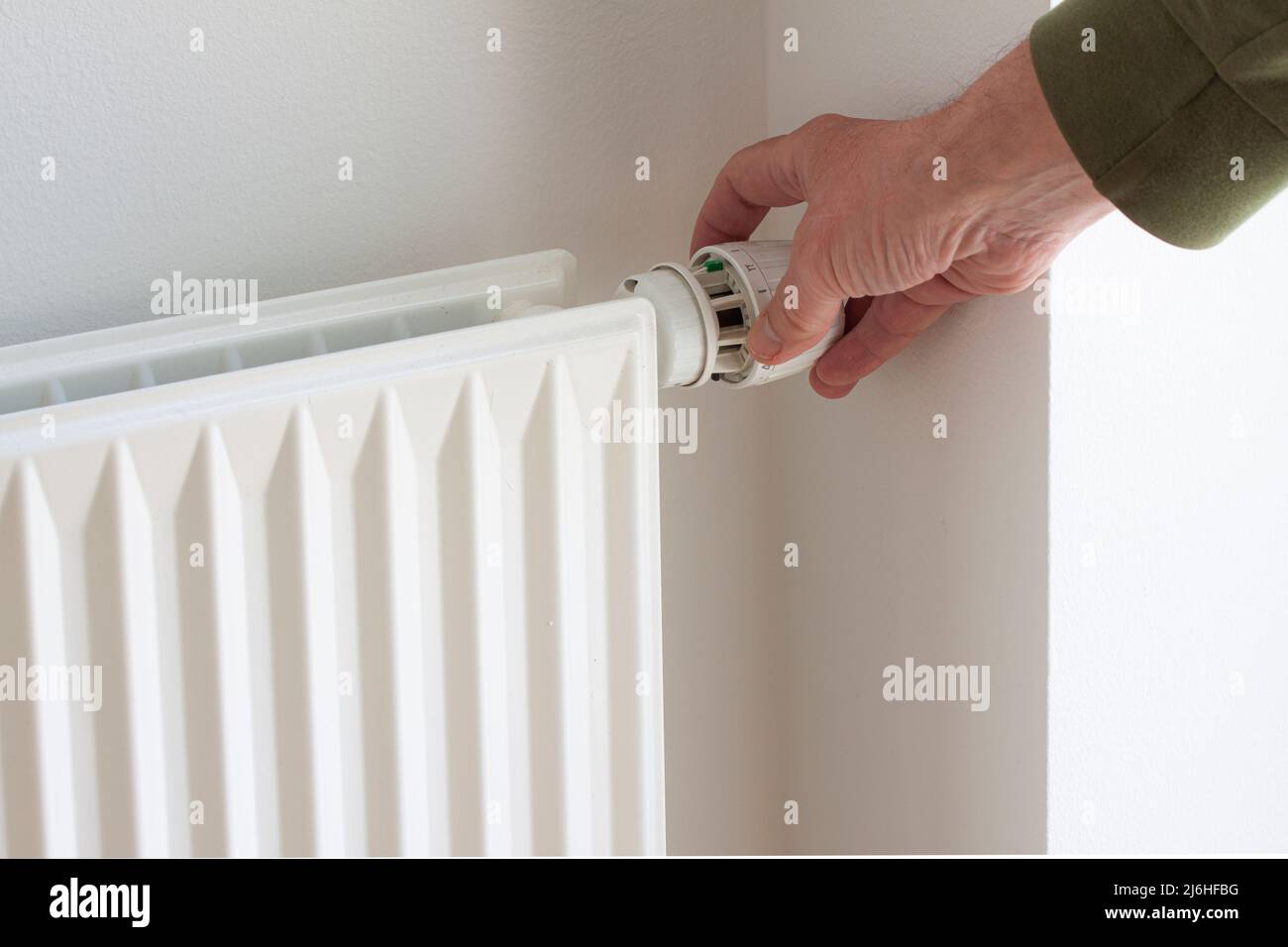 Hand turning down adjusting knob on thermostat on radiator valve to save energy due to heating cost price. Temperature control. Stock Photo