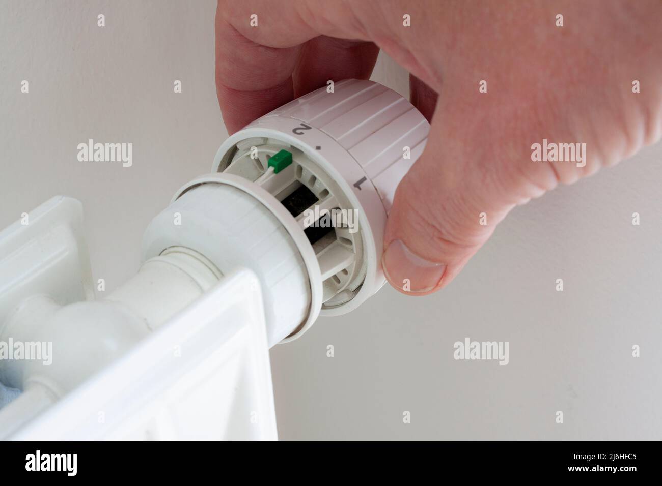 Hand turning down adjusting knob on thermostat on radiator  valve to save energy due to heating cost price. Temperature control. Close up image. Stock Photo
