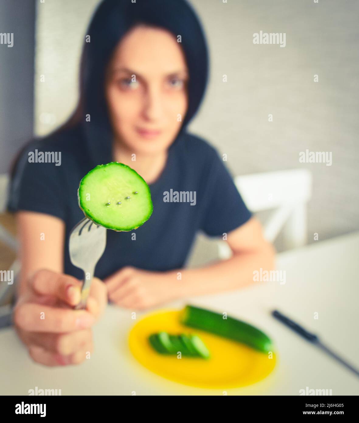 Young attractive woman show cucumber on fork. Vegetarian diet, loosing weight and slimming concept copypaste vertical background Stock Photo