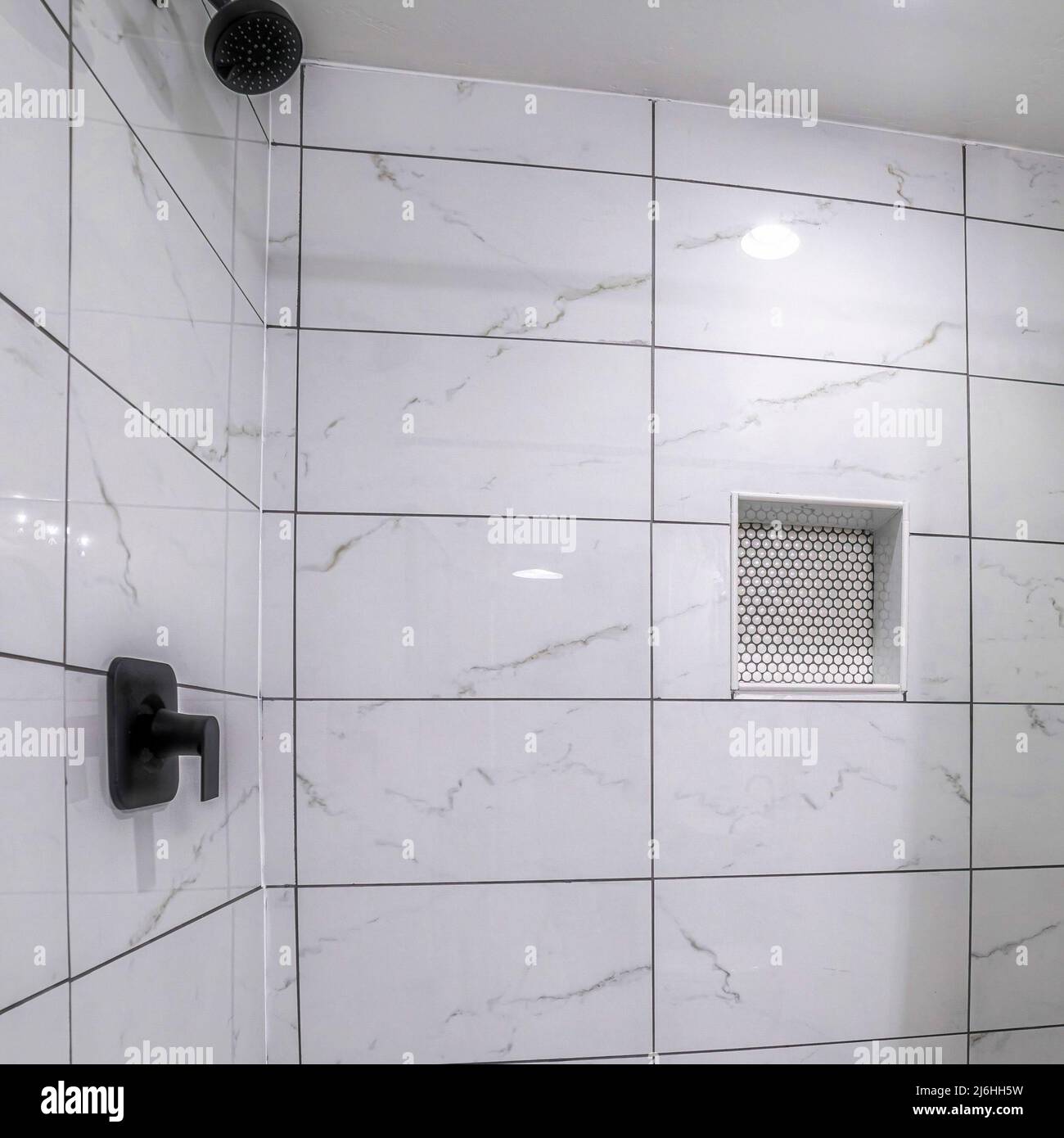 Square Shower stall with mosaic tiles flooring and marble tiles surround with black grout Stock