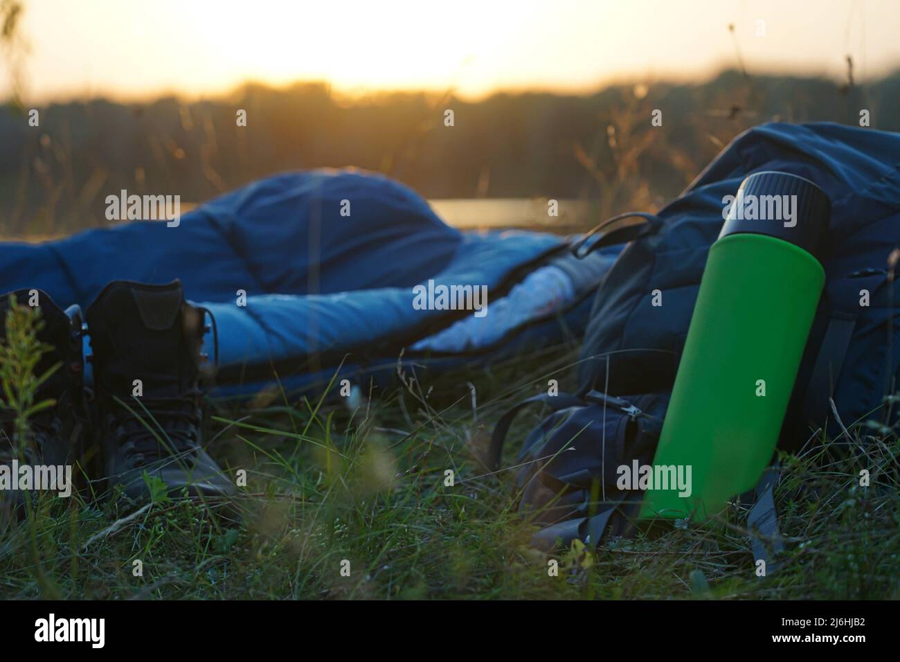 The thermos lies near the backpack and sleeping bag on the grass