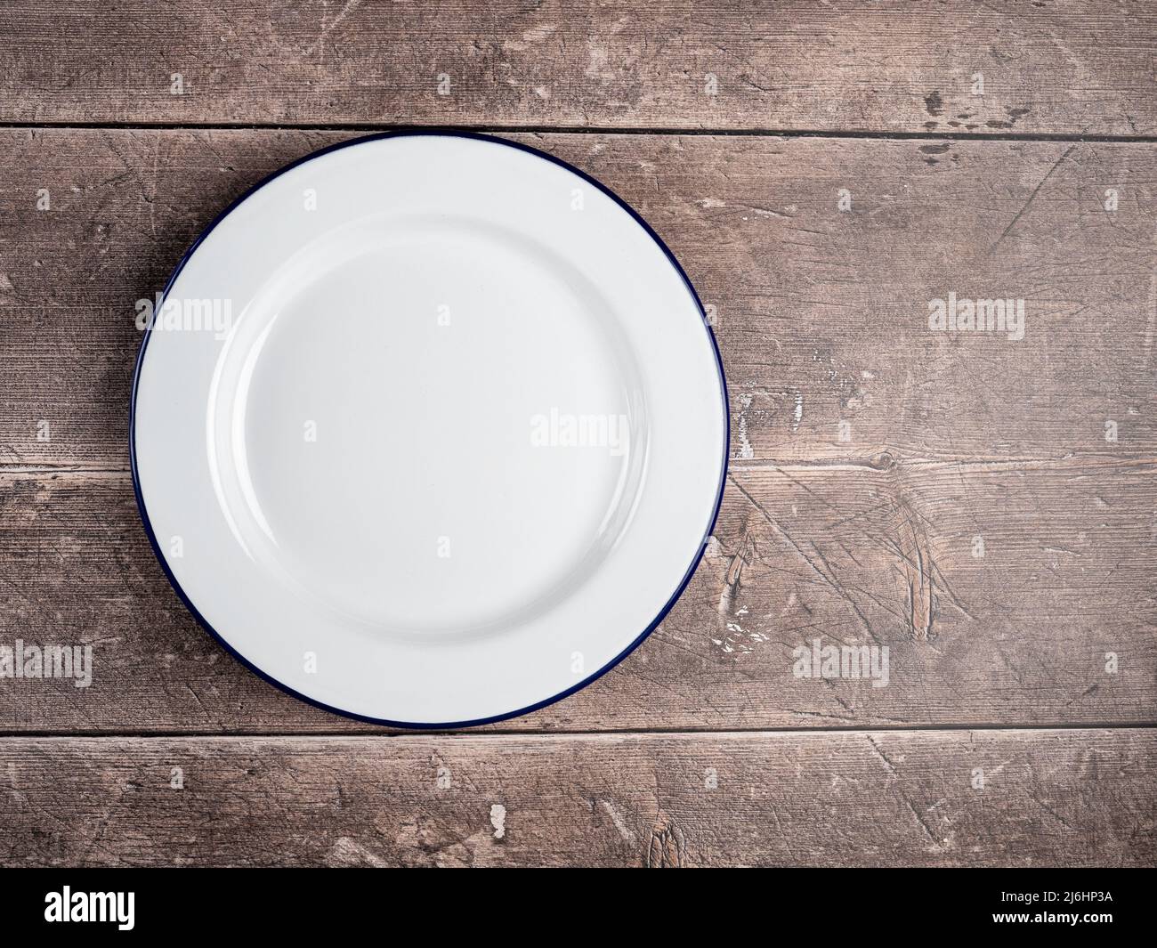 isolated traditional White Enamel plate with navy blue rim used for baking and cooking on a rustic wooden table background Stock Photo