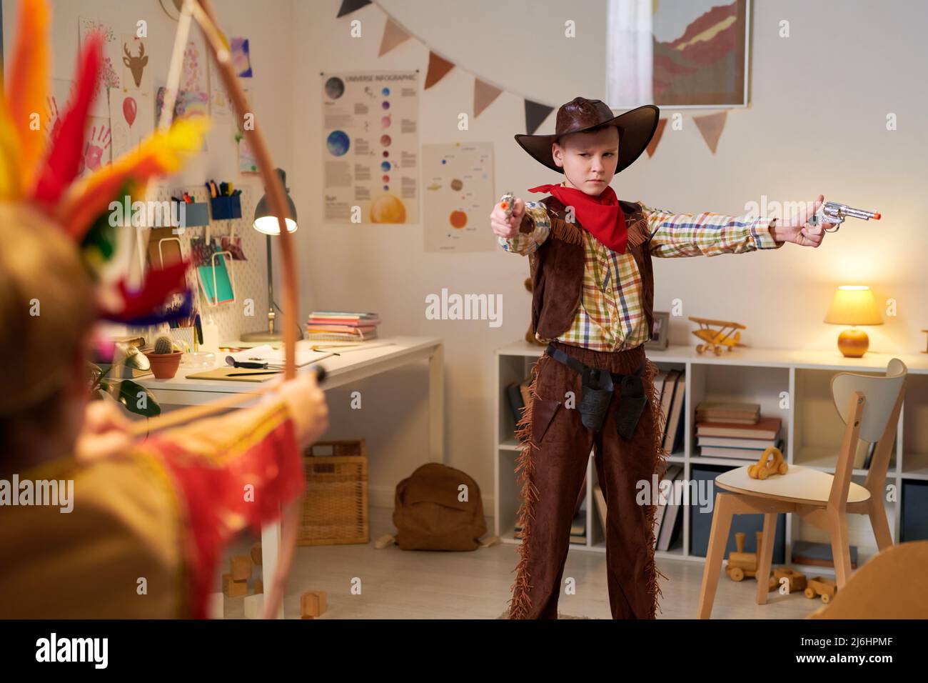 Little schoolboy in costume of cowboy holding two guns during play at home or classroom in school or while posing for commercial Stock Photo