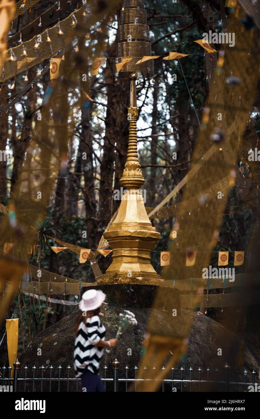 A female Buddhist offering flowers to the golden stupa on a top of a mountain. North Thailand. Focus on stupa. Stock Photo