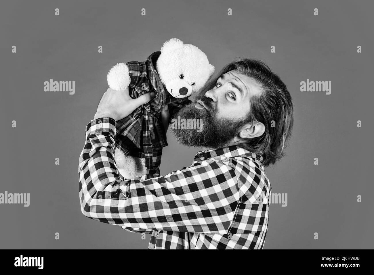 brutal bearded man wear checkered shirt having lush beard and moustache kiss teddy bear toy, love Stock Photo