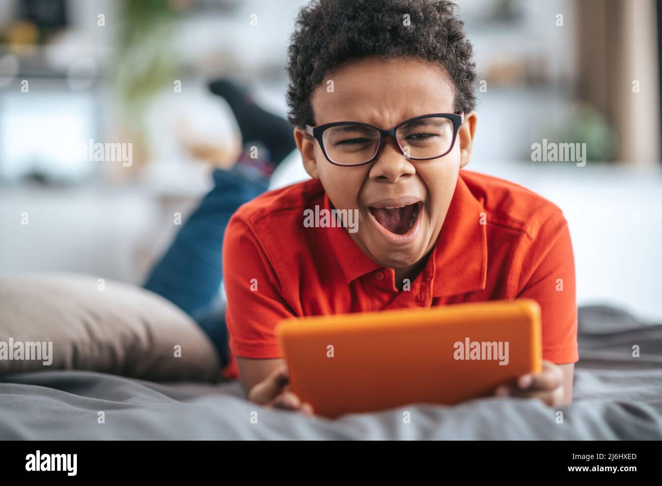 A boy in orange tshirt watching something online and yawning Stock Photo
