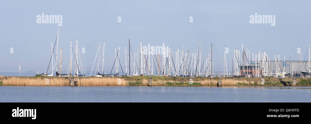 Cityscape of the 'Werkhaven' in Lemmer, Netherlands with shipyard, silos, storage sheds, lighthouse, large cargo ship and sailing boats. Widescreen Stock Photo