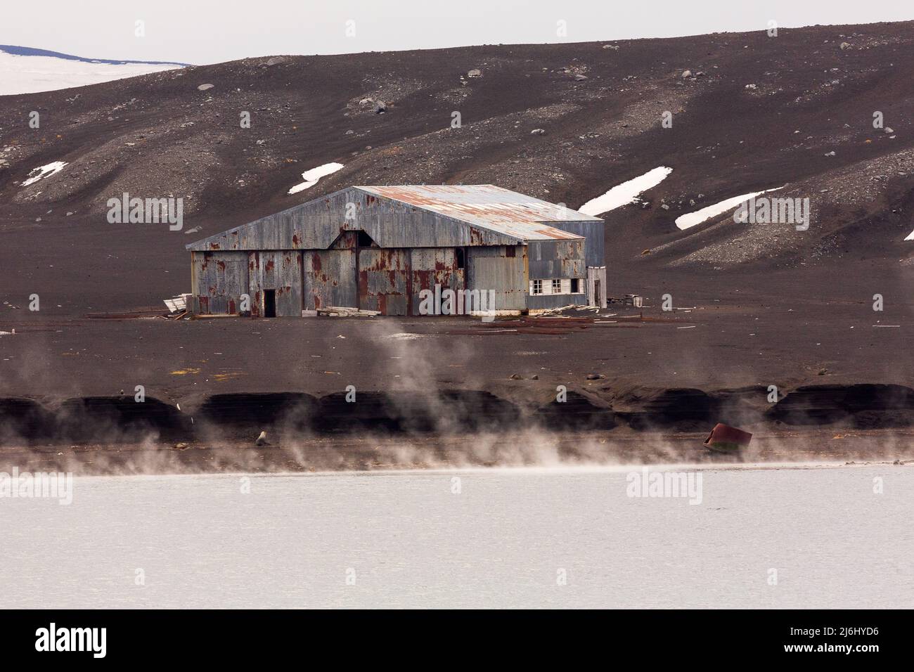 steam rises on the frozen beach in front of the dilapidated aircraft hanger of the abandoned scientific station of deception island antarctica Stock Photo