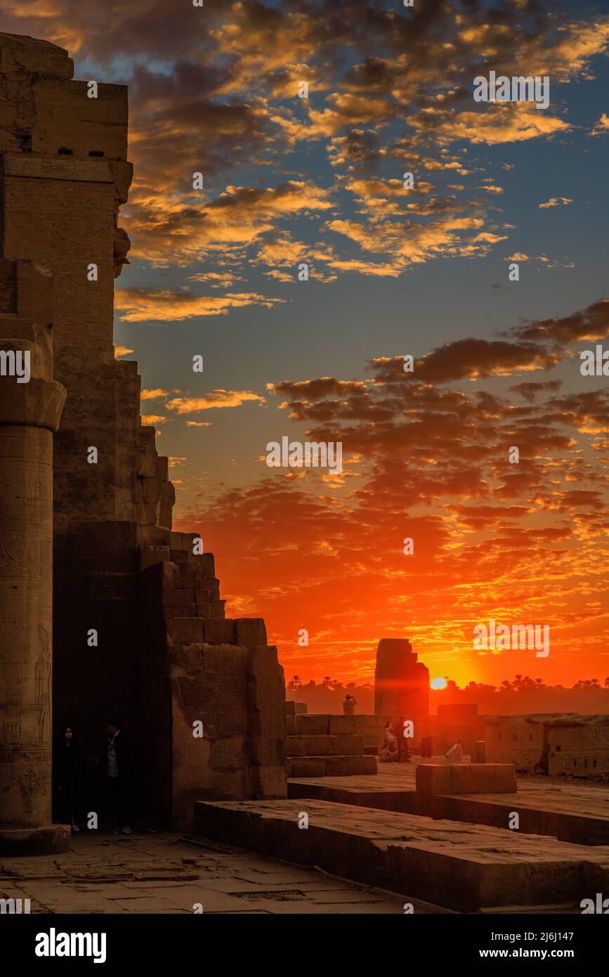 a distant photographer on the walls of the deserted kom ombo temple site in egypt takes a beautiful sunset scene Stock Photo