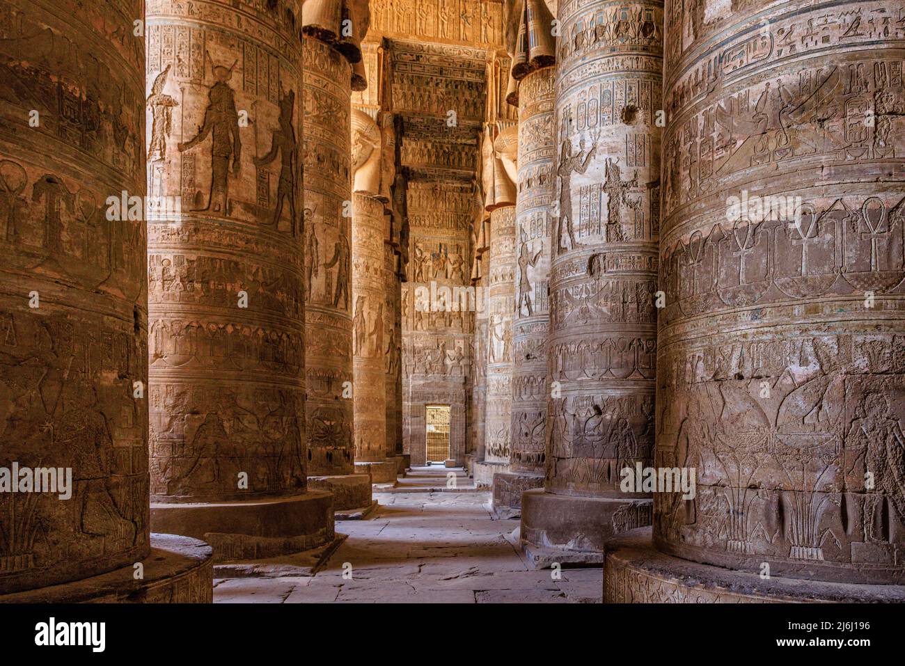 a small sunlit doorway at the end of two rows of huge columns covered in hieroglyphs in the large hypostyle hall of the temple of hathor dendera Stock Photo