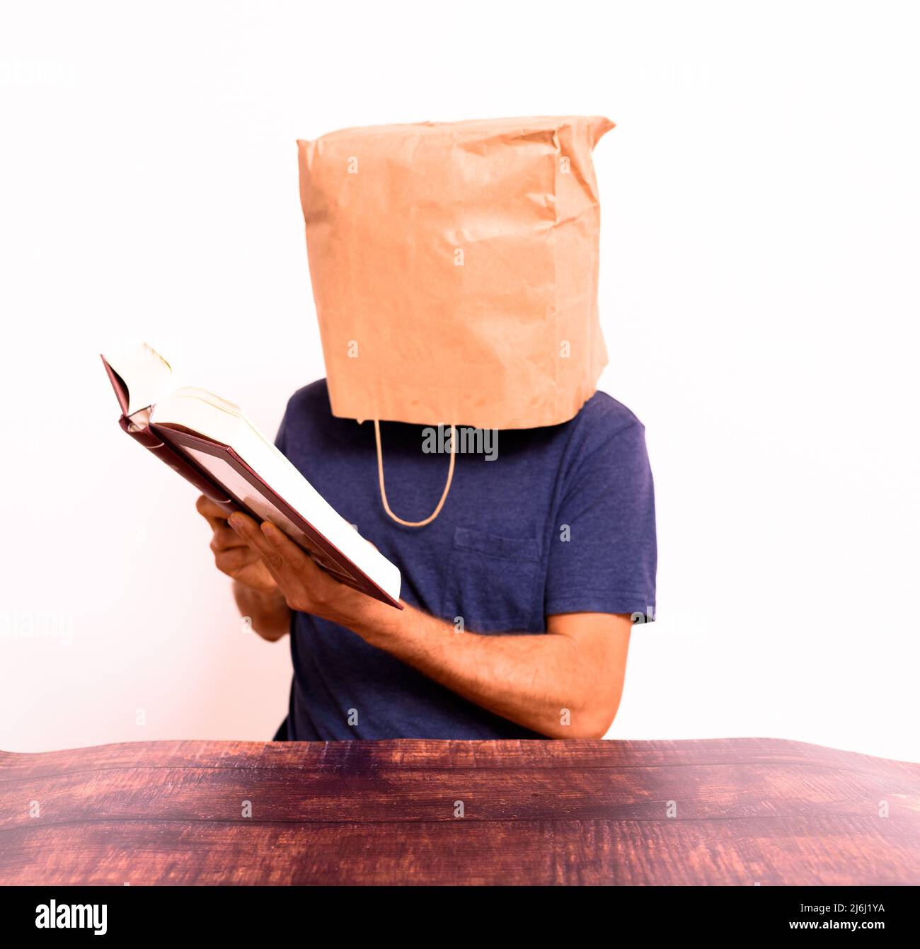 Funny man with his head covered with a paper bag reading and studying a book. Stock Photo