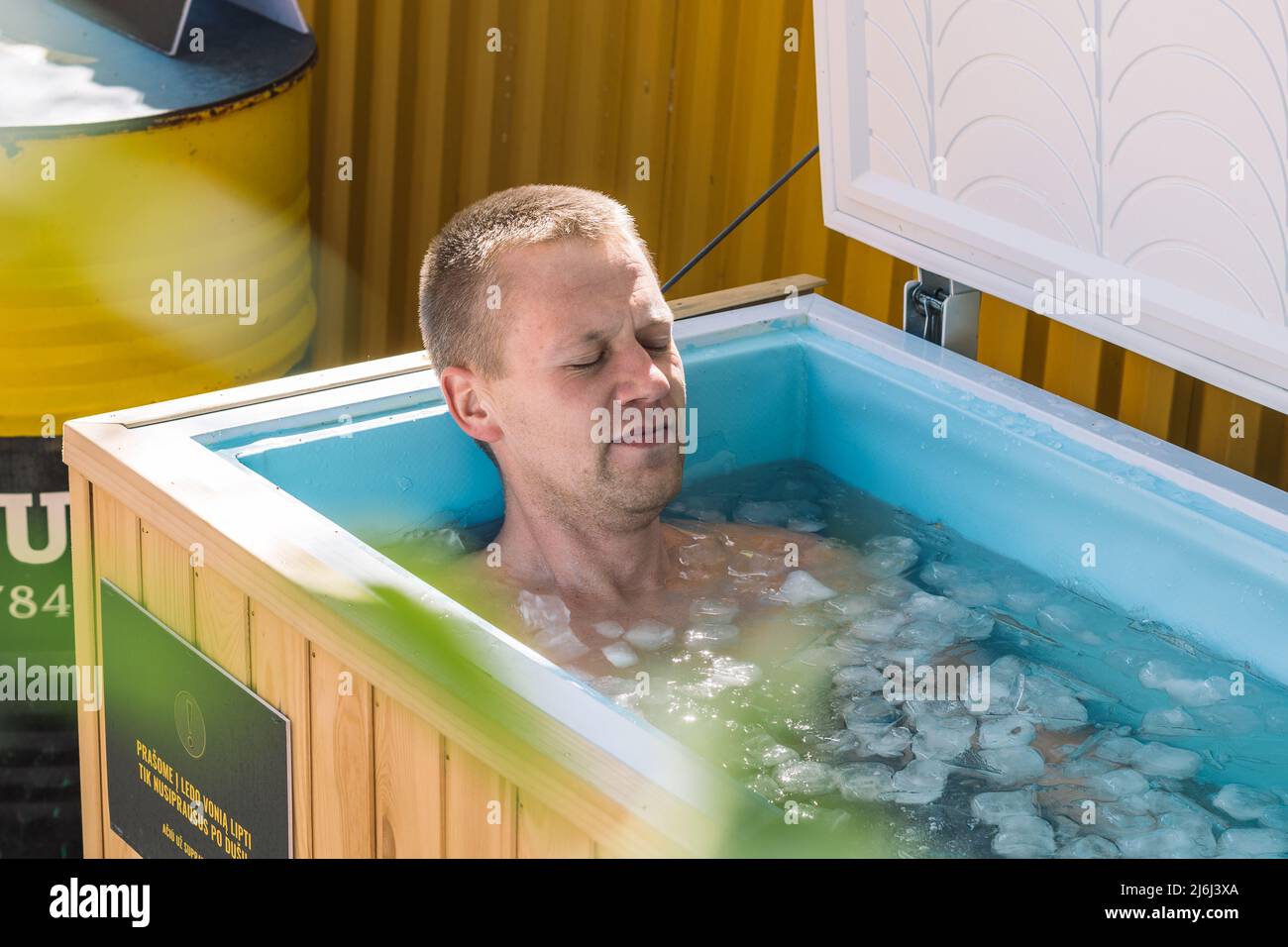 Boy or man with closed eyes bathing in the cold water among ice cubes