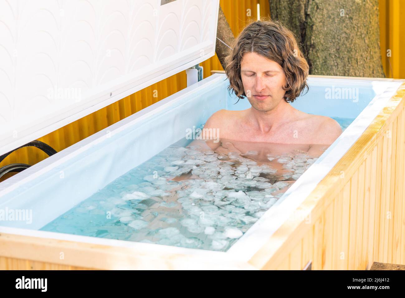 Boy or man with closed eyes bathing in the cold water among ice cubes