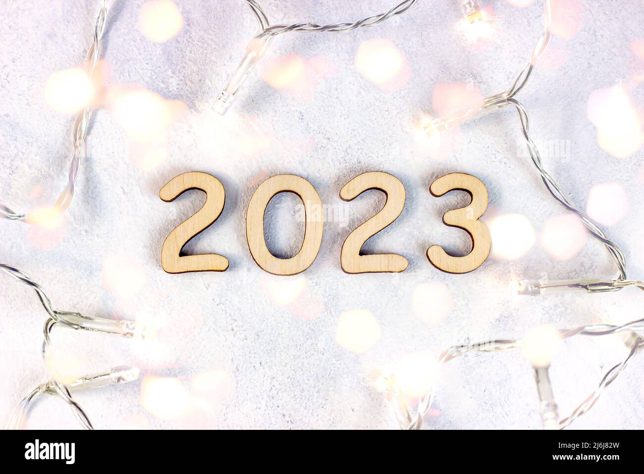 Wooden numbers 2023 silhouette with Christmas lights on light bokeh background. New Year beginning congratulations and planning concept. Stock Photo