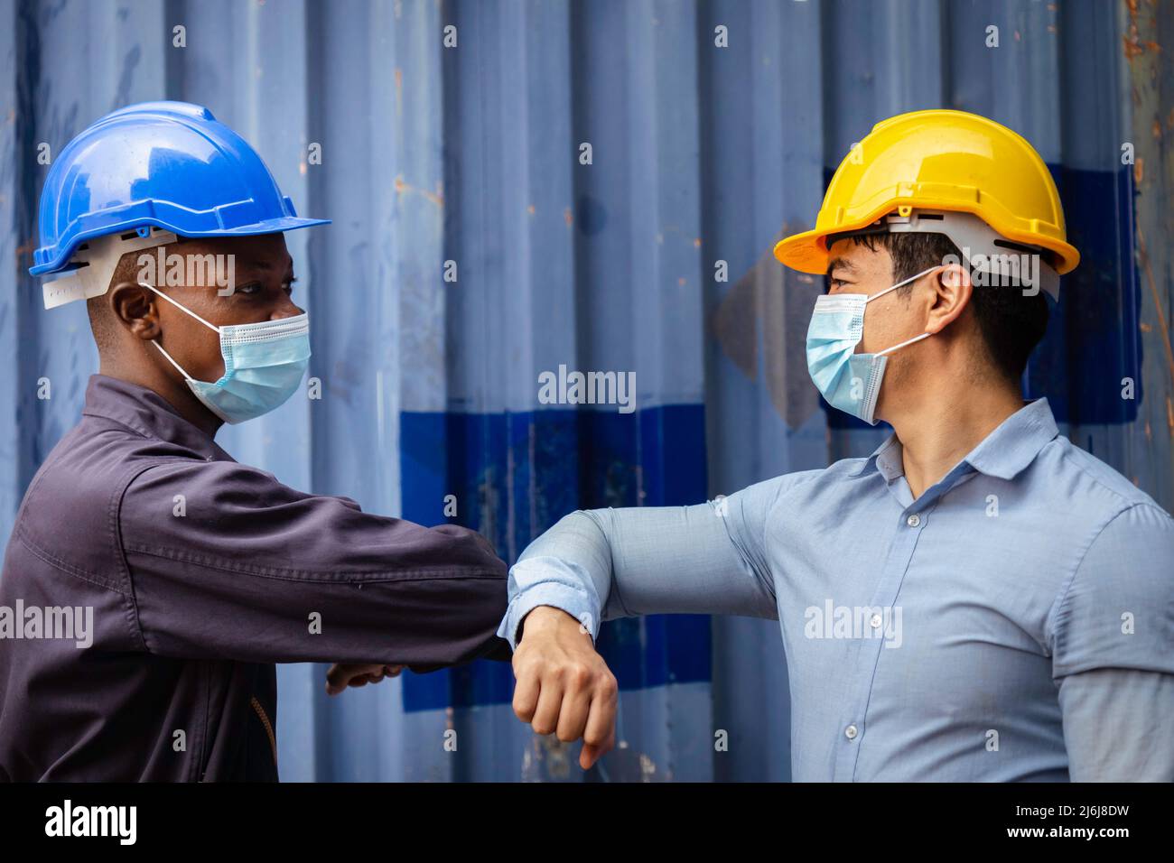 african engineer and caucasian businessman wearing face mask to protect from covid or coronavirus in cargo warehouse at the dock have greeting and tou Stock Photo