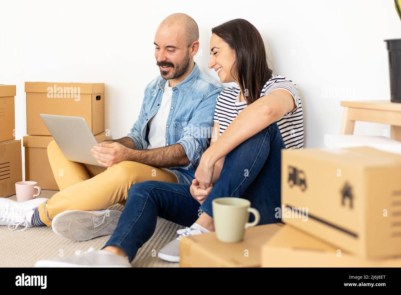 Happy young adult couple using laptop computer in new home Stock Photo