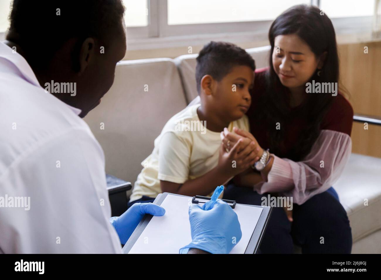 family psychologist. asian mother and her boy talk to african american psychotherapist doctor during therapy session at the hospital. Stock Photo
