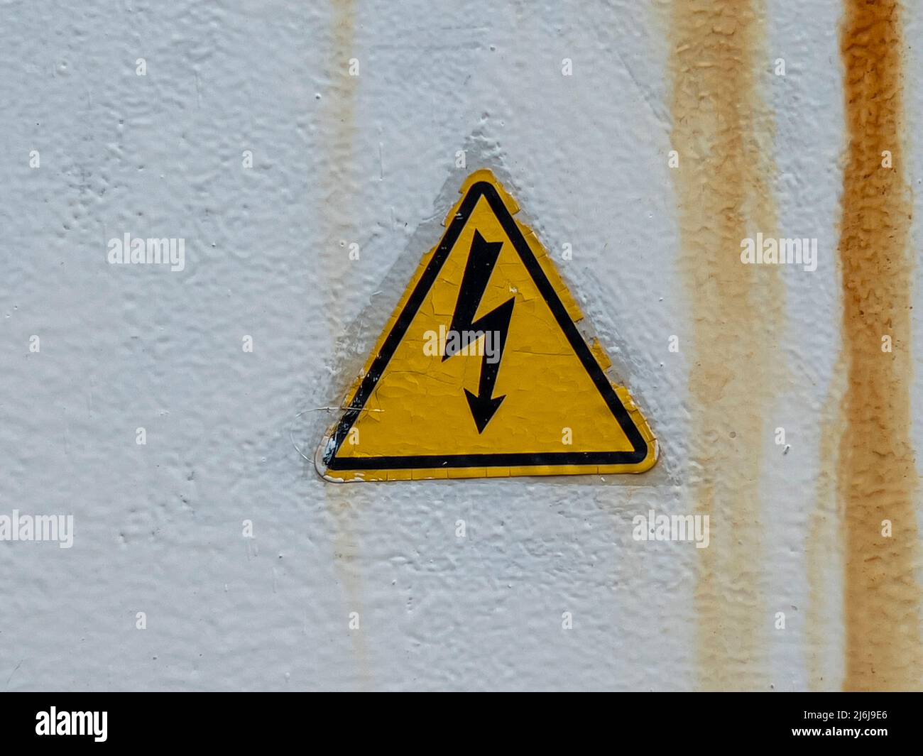 High Voltage sign. Old risk of electric shock triangle symbol on weathered cracked background with copy space. Danger symbol. Black in yellow triangle Stock Photo