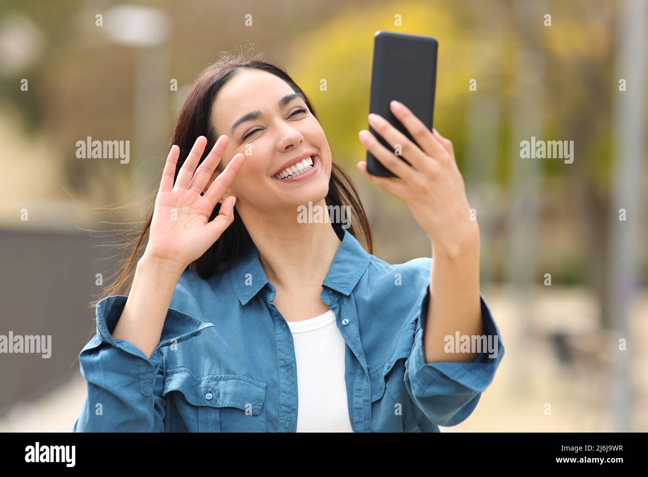 Happy woman greeting having videocall or taking slefie on phone in a park Stock Photo