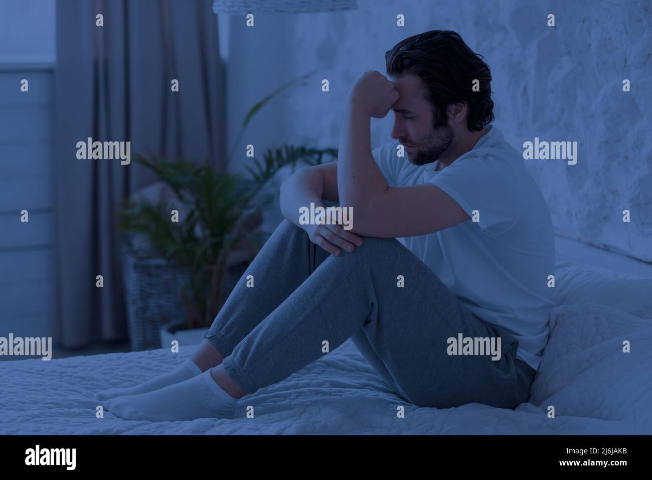 Sleepless millennial man feeling down at night, bedroom interior Stock Photo