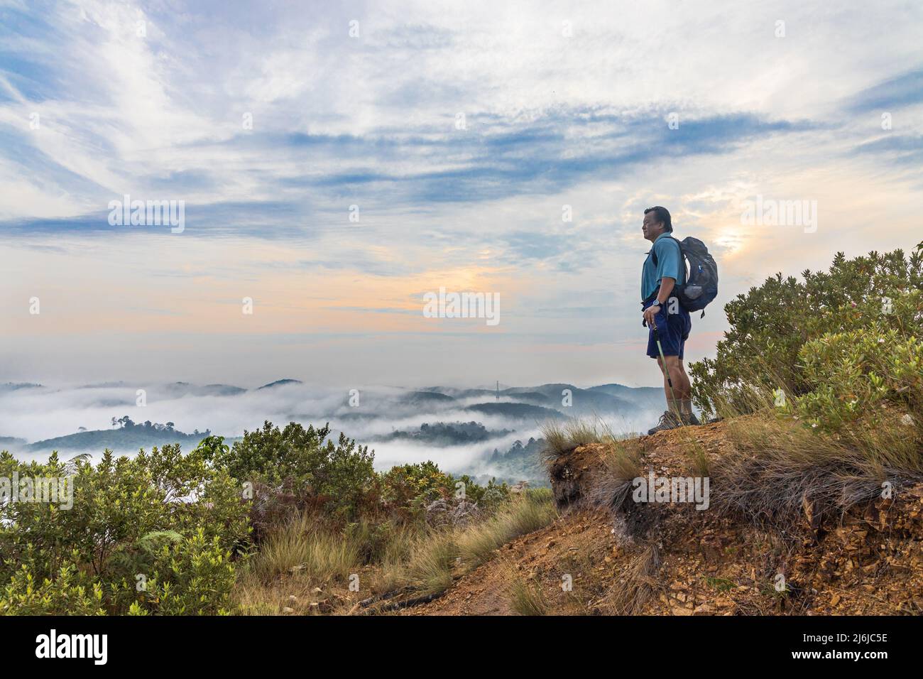 Hiker Asian man standing on peak of mountain admiring cloud scape and sunrise Stock Photo