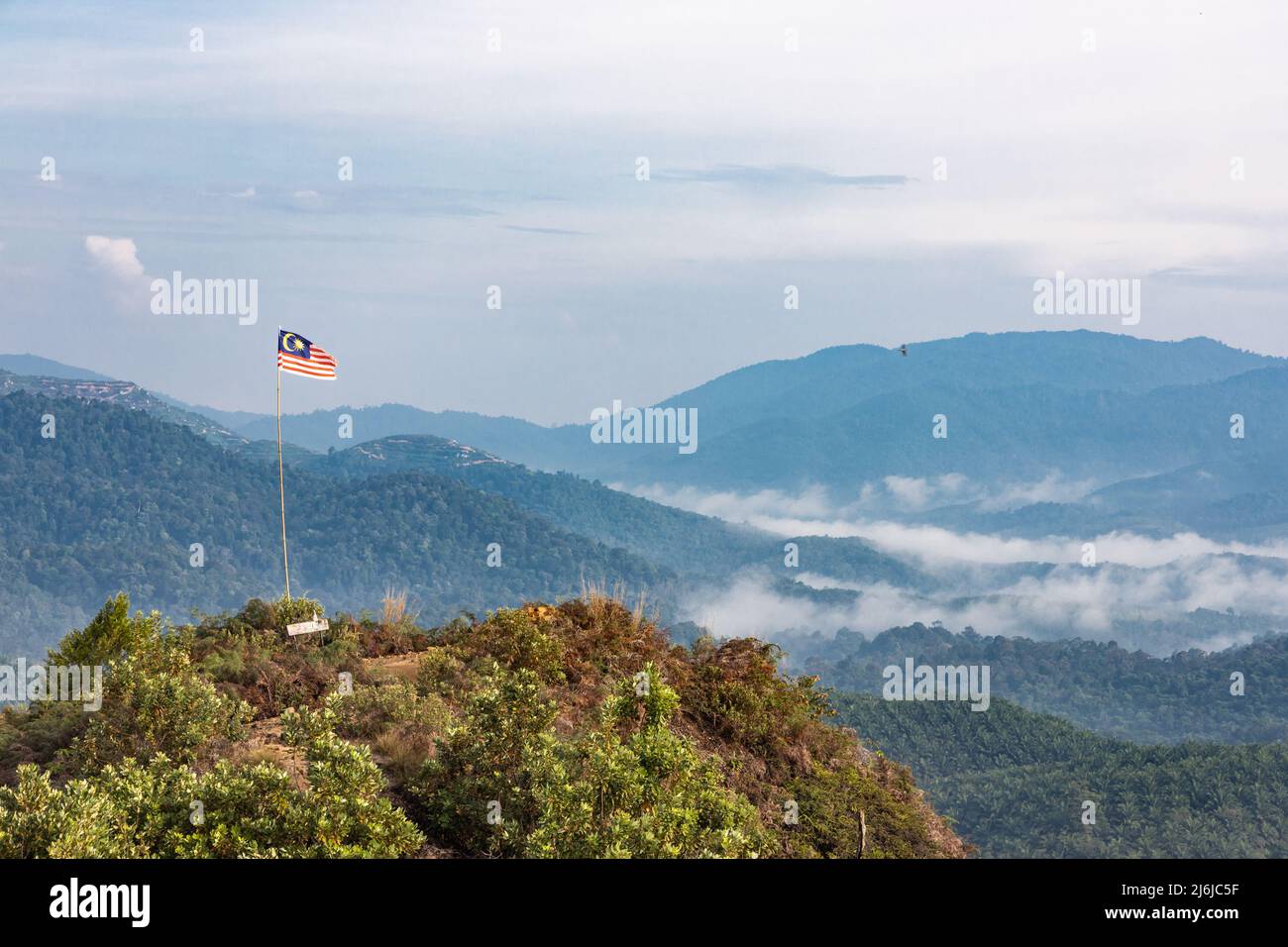 Malaysia flag flying on pole on mountain highland against sea of cloud and blue sky Stock Photo