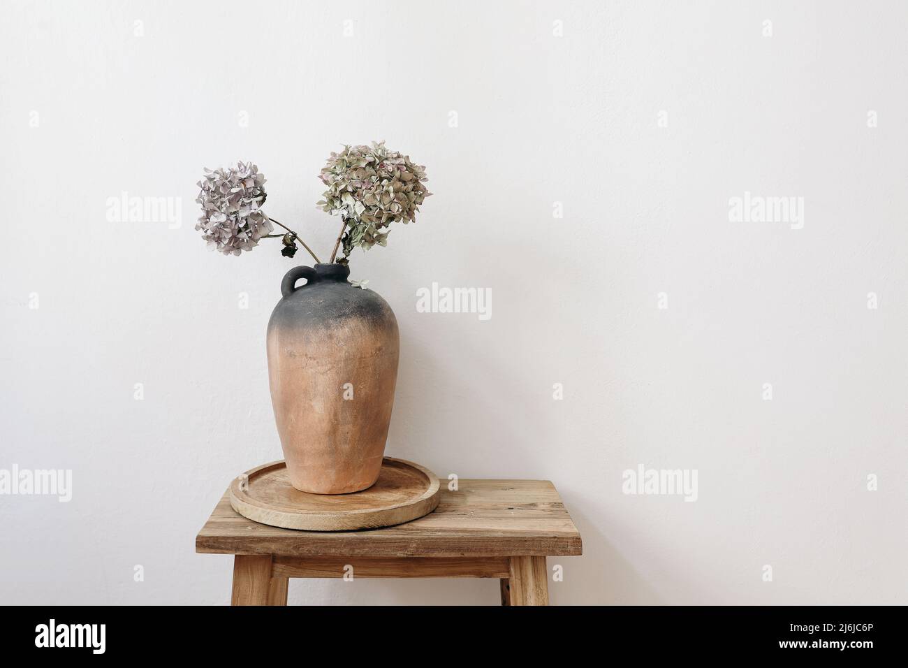 Elegant minimal summer, fall still life photo. Rustic clay vase, pitcher with hydrangea flowers on old wooden stool, console table. White wall Stock Photo