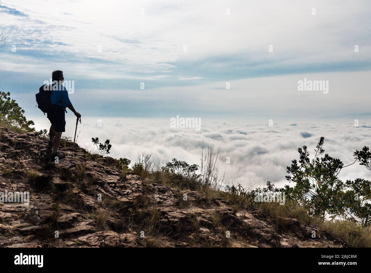 Hiker Asian man in silhouette standing on peak of mountain admiring cloud scape and sunrise Stock Photo