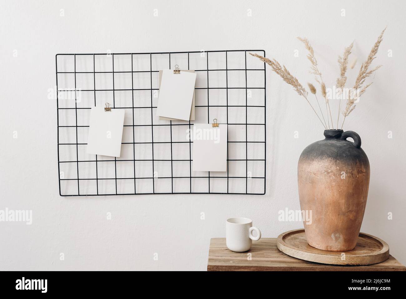Black metal mesh noticeboard, bulletin board with blank memo cards mockups. Elegant home office interior concept. Vase with dry lagurus grass and cup Stock Photo