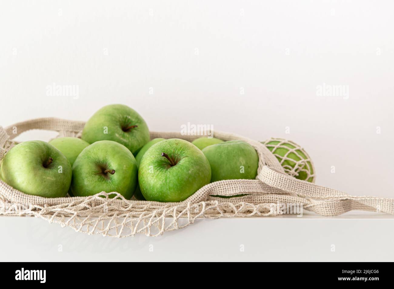 Green apples in a string bag on a white background. Stock Photo